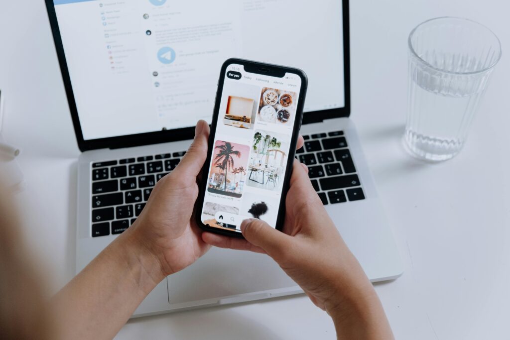 Henkilö selaamassa visuaalista sisältöä puhelimella läppärin äärellä